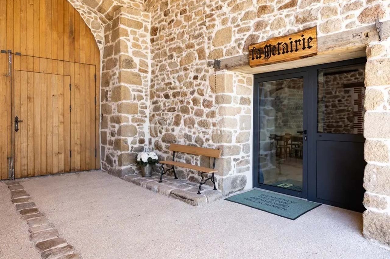 Entrée d'un bâtiment en pierre avec une porte vitrée, un banc en bois et une enseigne ’La Métairie’.