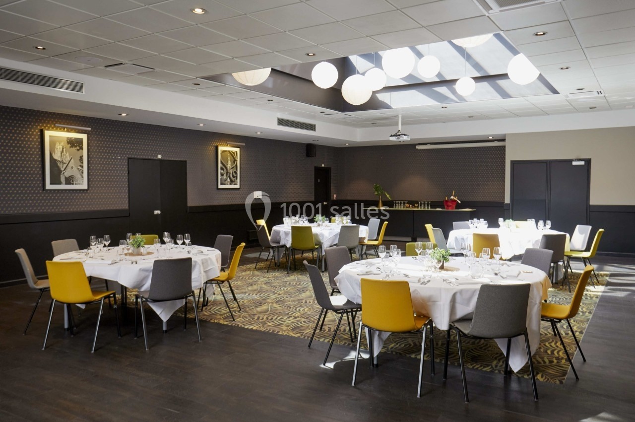 Salle de réception lumineuse avec tables rondes dressées, chaises colorées et décor sobre.