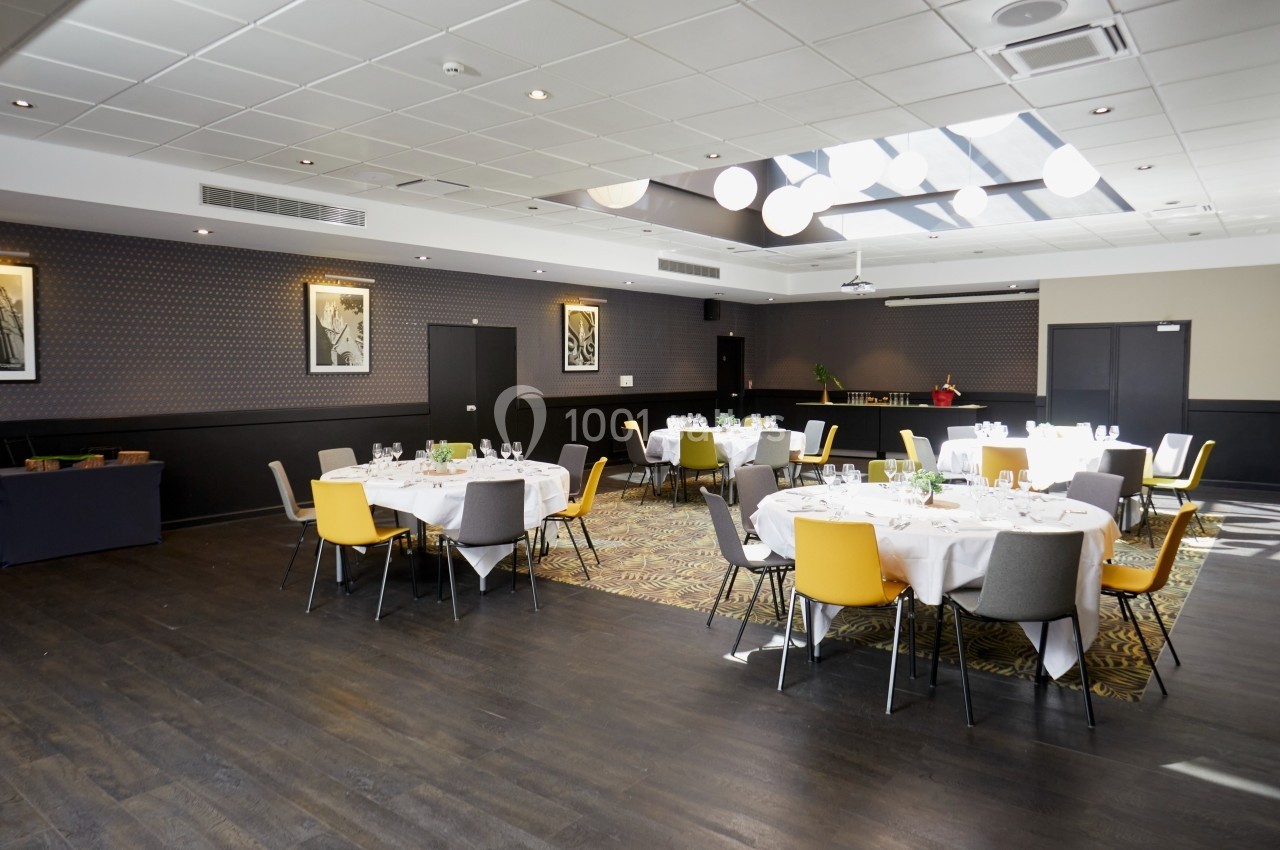 Salle de réception lumineuse avec tables rondes dressées, chaises colorées et décorations modernes.