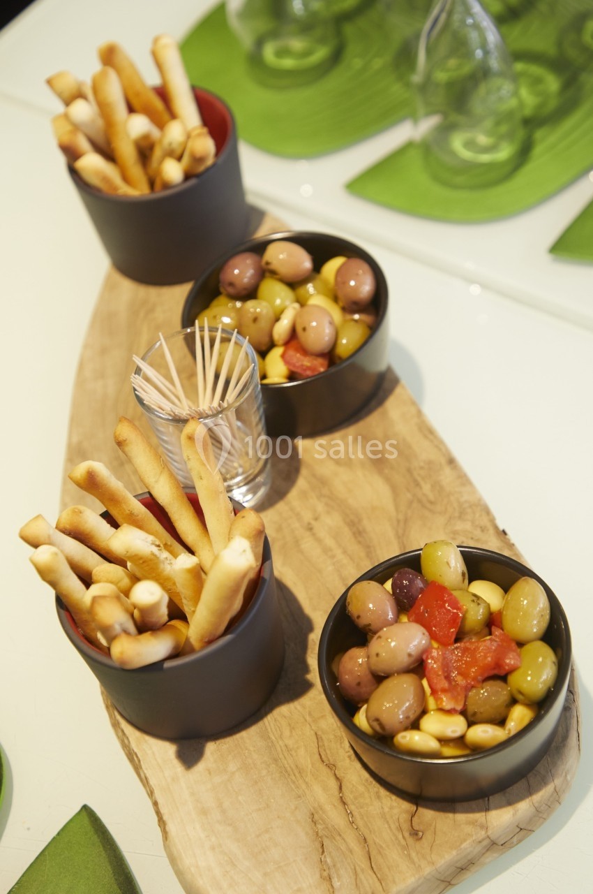 Assortiment d'olives, tomates et gressins disposés dans des bols sur une planche en bois.