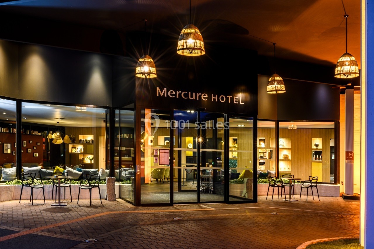 Entrée éclairée d'un hôtel avec des tables extérieures et des luminaires suspendus, vue de nuit.