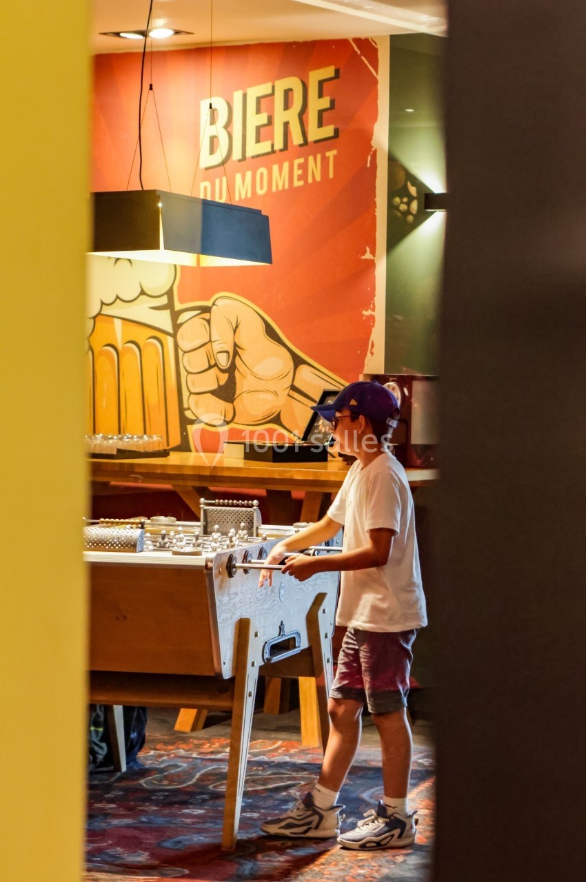 Location salle Marcq-en-Baroeul (Nord) - Mercure Lille Marcq en Baroeul #5 Un enfant joue au baby-foot dans un bar avec une affiche ’Bière du moment’ en arrière-plan.