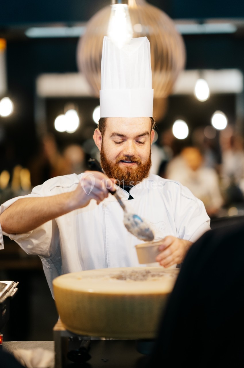 Location salle Marcq-en-Baroeul (Nord) - Mercure Lille Marcq en Baroeul #11 Un chef en tenue blanche sert un plat à partir d'une grande meule de fromage dans un environnement lumineux.