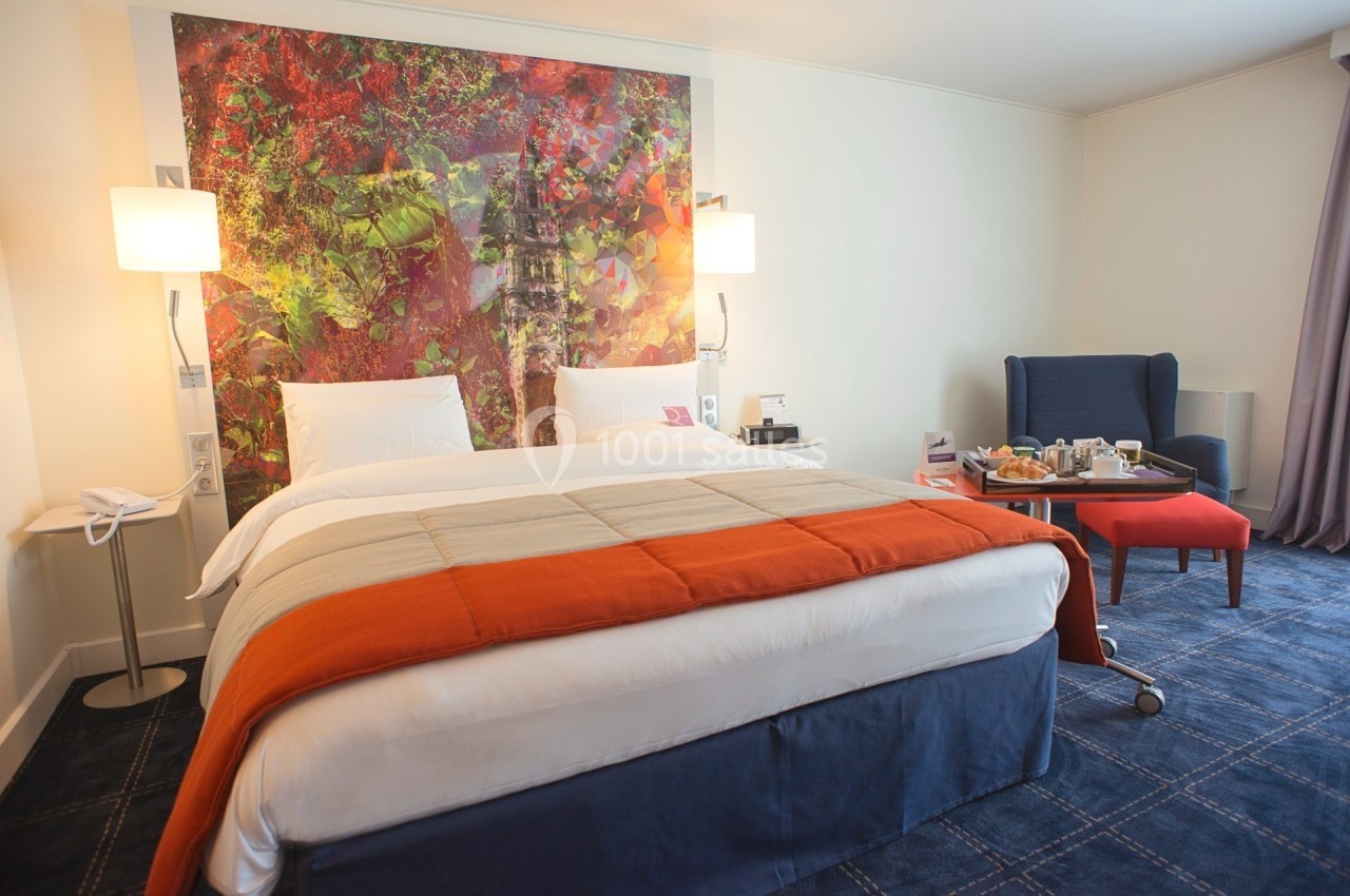 Location salle Marcq-en-Baroeul (Nord) - Mercure Lille Marcq en Baroeul #21 Lit double avec couvre-lit orange dans une chambre d'hôtel moderne, décorée avec un tableau coloré au mur.