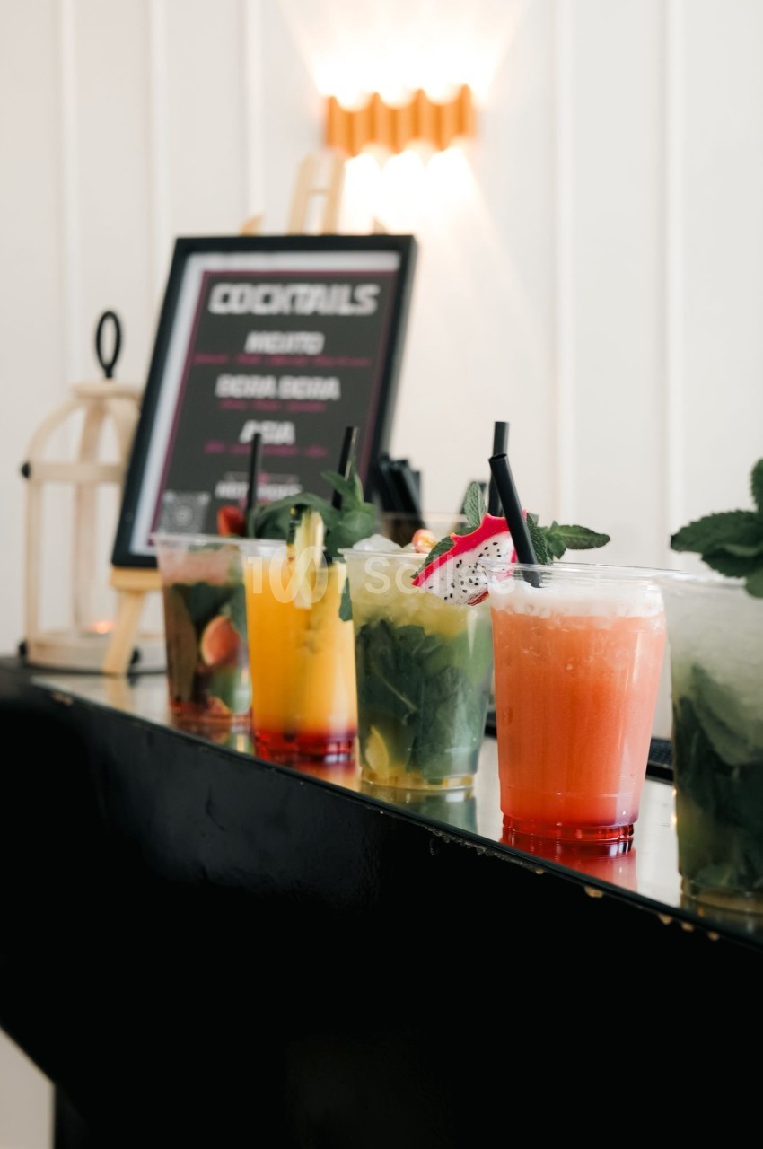 Verres de cocktails variés avec garnitures colorées alignés sur un comptoir noir devant un panneau de menu.