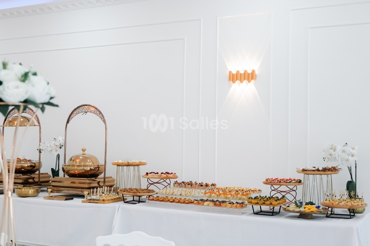 Table garnie de plats et amuse-bouches variés, disposés sur des présentoirs dans une salle lumineuse et élégante.