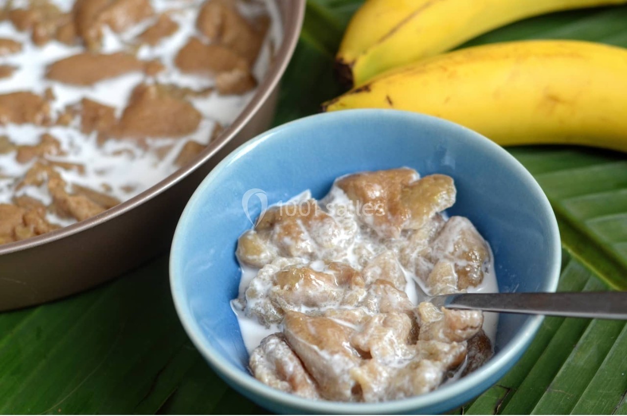 Bol de bananes cuites dans du lait de coco, avec une casserole similaire en arrière-plan et deux bananes jaunes à côté.