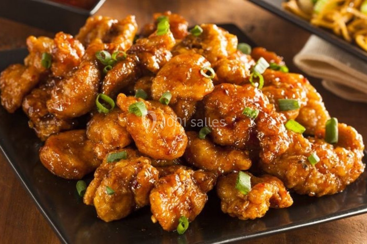 Poulet croustillant caramélisé garni de ciboulette, servi sur une assiette noire.