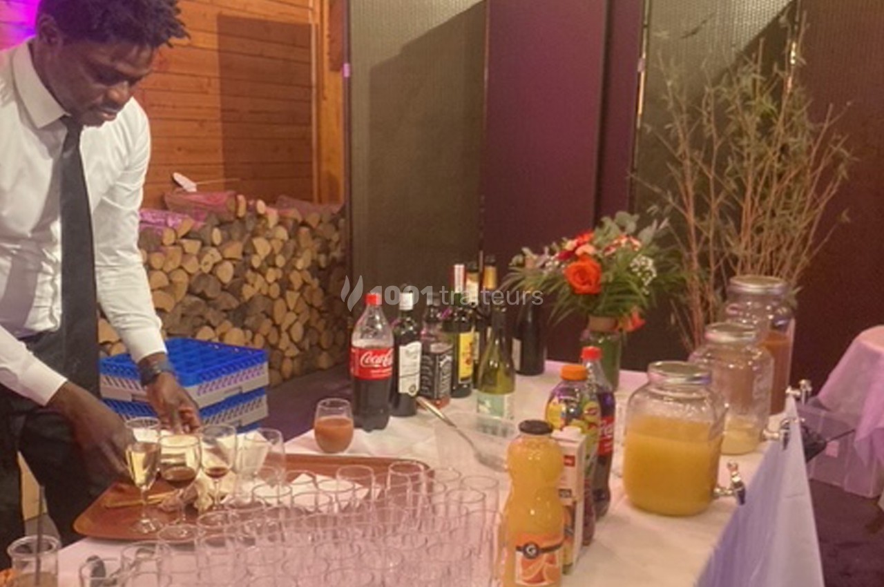 Un serveur prépare des verres de champagne sur un plateau devant un bar garni de boissons et de décorations florales.