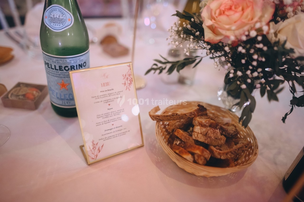 Bouteille d'eau pétillante, menu, panier de pain et bouquet de fleurs sur une table dressée.