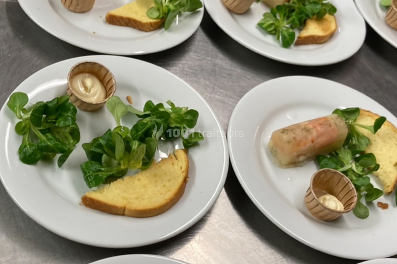 Assiette composée de mâche, tranche de pain, rouleau de printemps et sauce en pot individuel, sur une table en inox.
