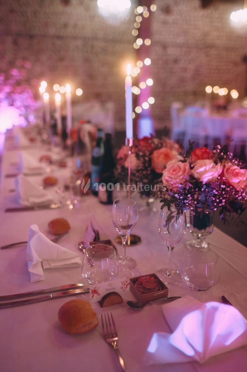 Table de réception élégamment dressée avec bougies allumées, fleurs roses et vaisselle raffinée dans une ambiance tamisée.