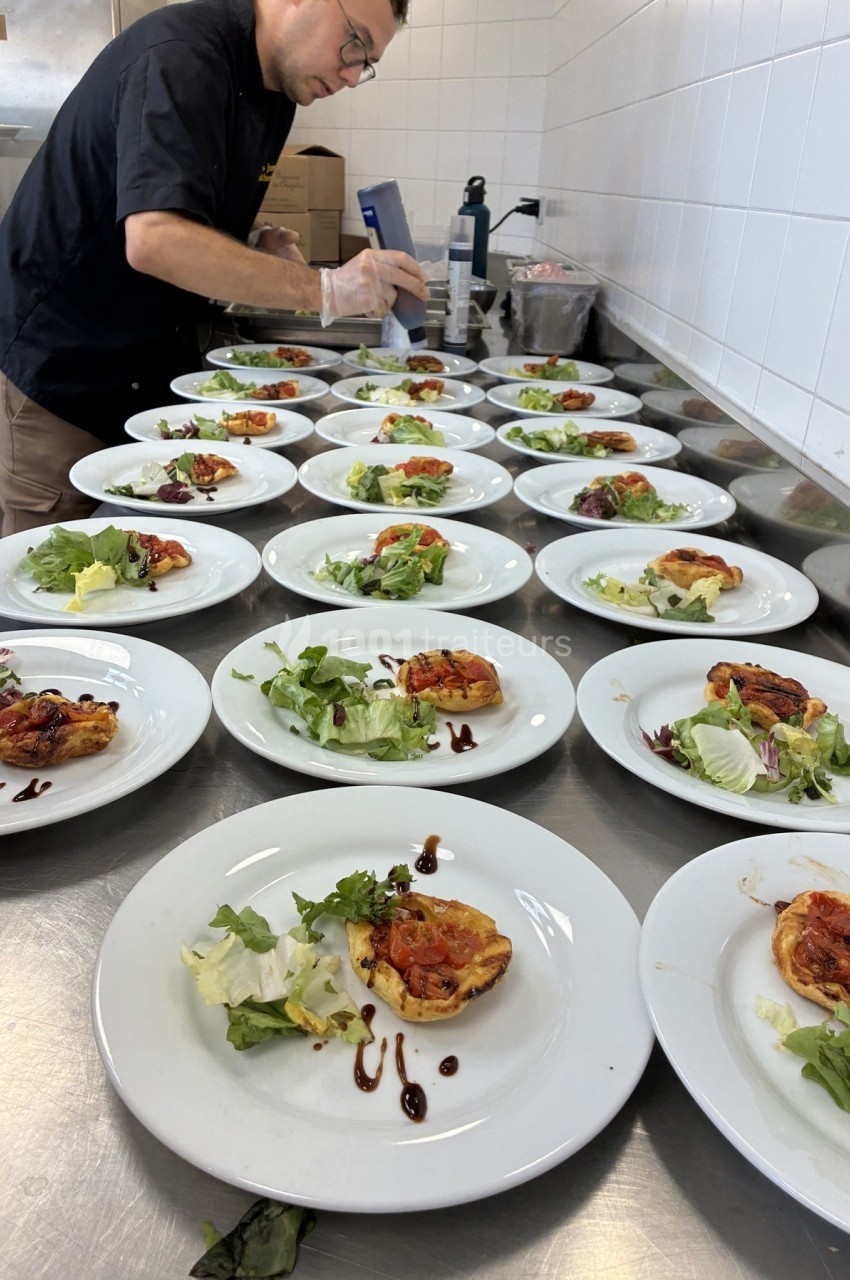 Un chef prépare des assiettes contenant une tartelette salée, de la salade verte et un filet de sauce balsamique.