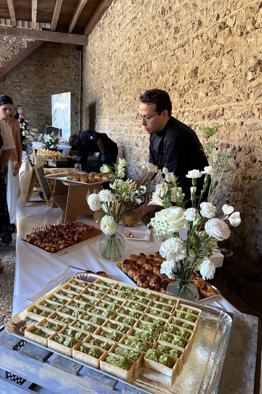 Un traiteur prépare un buffet avec des fleurs blanches en décoration dans un espace en pierre.