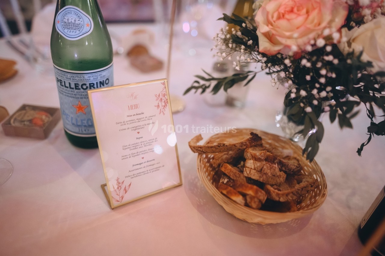 Menu imprimé sur une table décorée avec une bouteille d'eau, un panier de pain et un bouquet de fleurs.