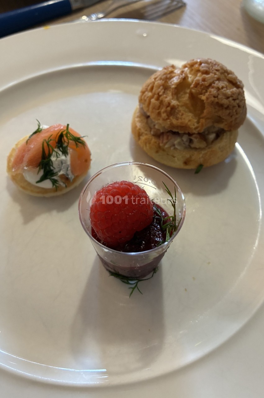 Assortiment de trois amuse-bouches : verrine aux fruits rouges, bouchée au saumon et choux garni sur une assiette blanche.