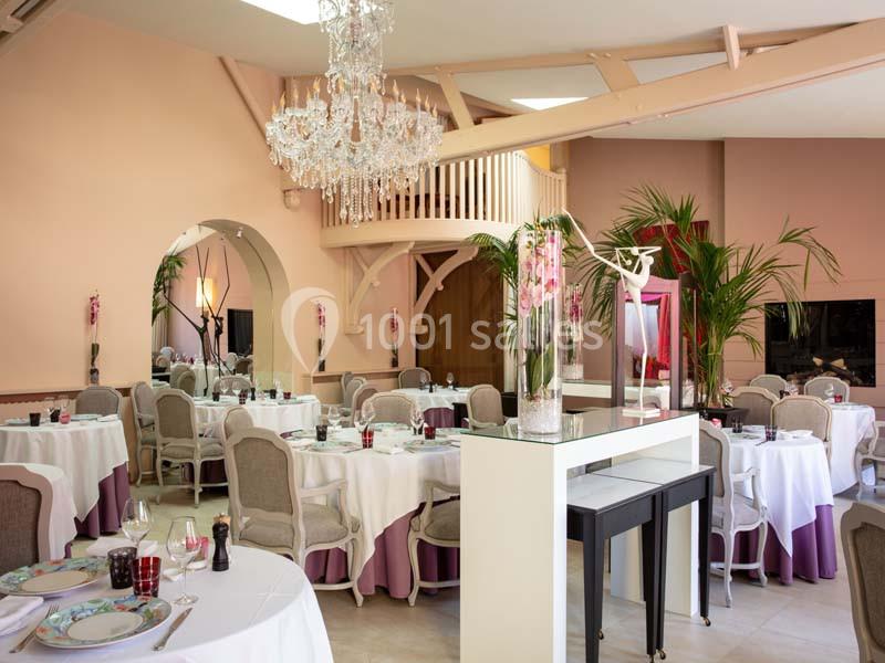 Salle de restaurant élégante avec tables dressées, lustre en cristal, plantes et mezzanine en bois clair.