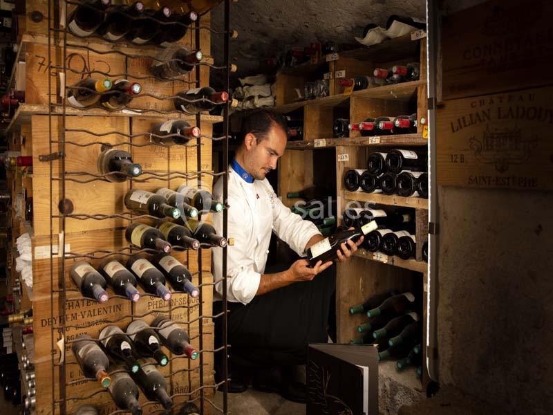 Un homme examine une bouteille de vin dans une cave remplie d'étagères contenant des bouteilles.