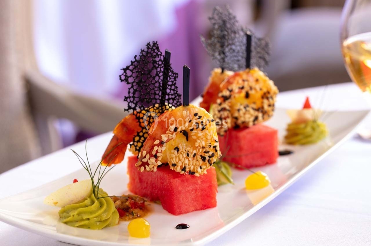 Assiette gastronomique avec crevettes en croûte de sésame, pastèque, purée d'avocat et décorations raffinées.