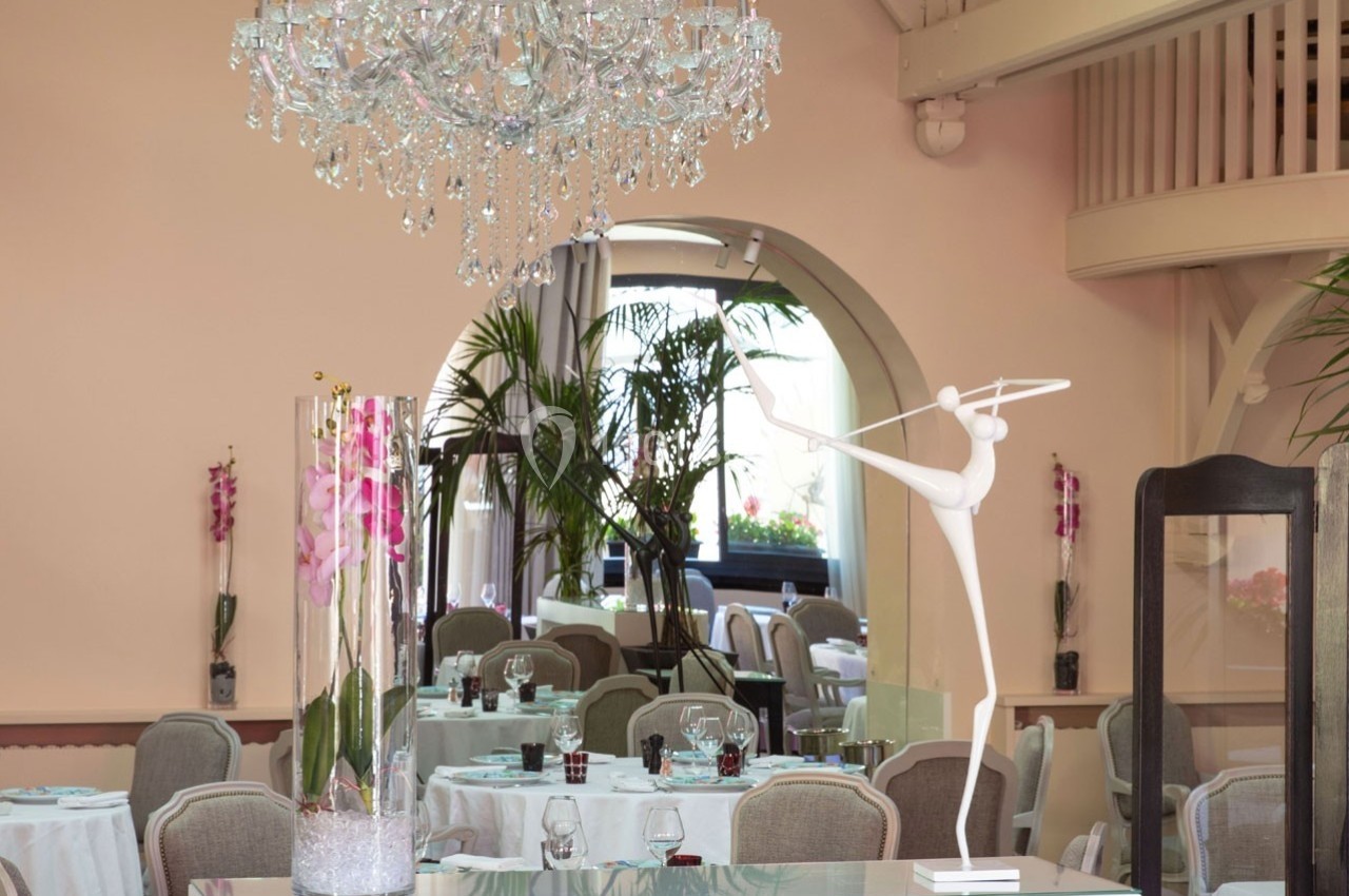 Salle de réception élégante avec tables dressées, lustre en cristal, décoration florale et sculpture moderne blanche.