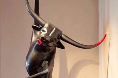 Sculpture moderne d'un taureau noir aux cornes longues et rouges, avec une posture dynamique et stylisée.
