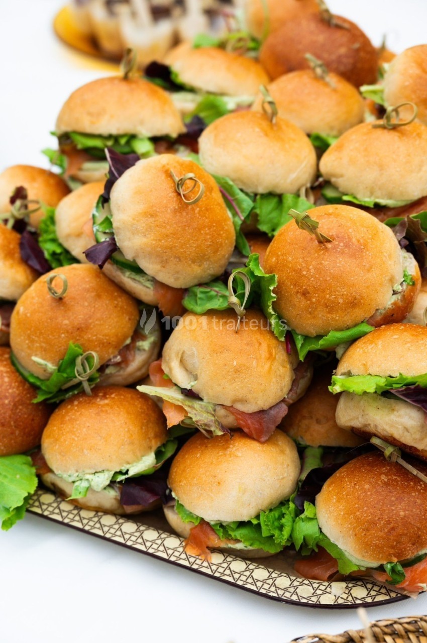 Plateau de mini-burgers garnis de salade, servis sur un support en bois, disposés pour un buffet ou un événement.