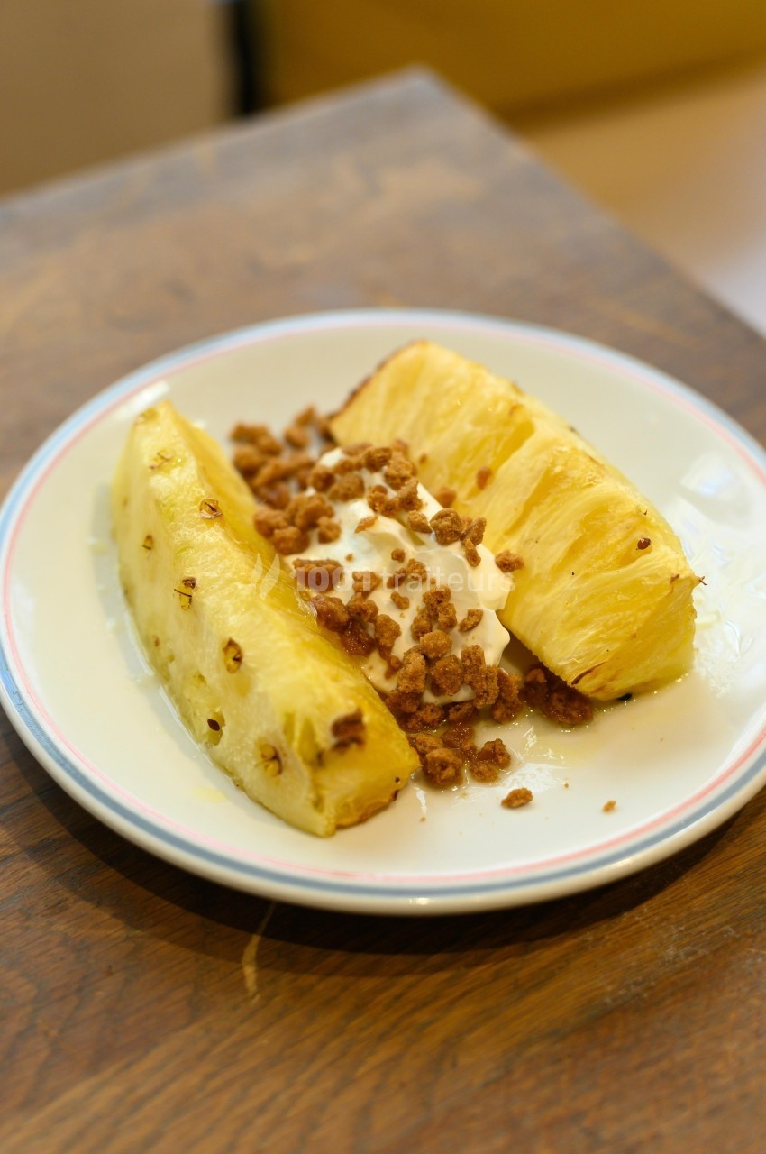 Tranches d'ananas frais servies avec de la crème et des éclats de noix sur une assiette blanche.