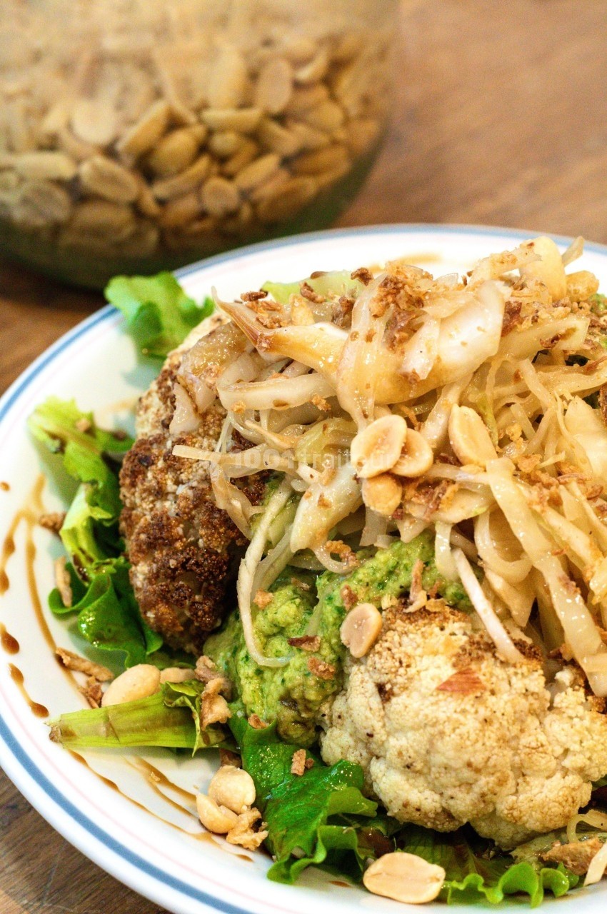 Assiette de chou-fleur rôti sur lit de salade, garnie de germes de soja, amandes effilées et sauce.