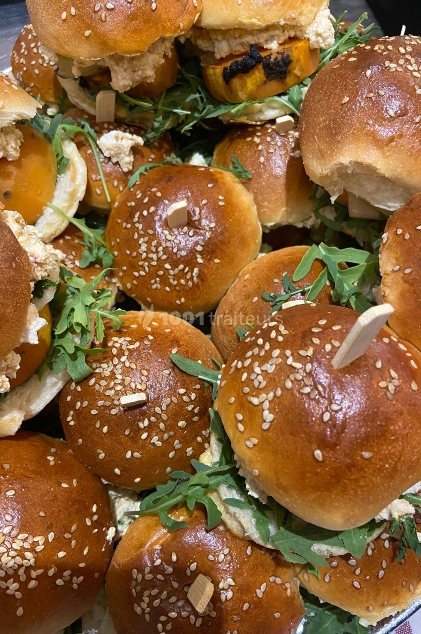 Assortiment de mini-burgers garnis de roquette, fromage et autres ingrédients, servis sur des pains briochés aux graines de…