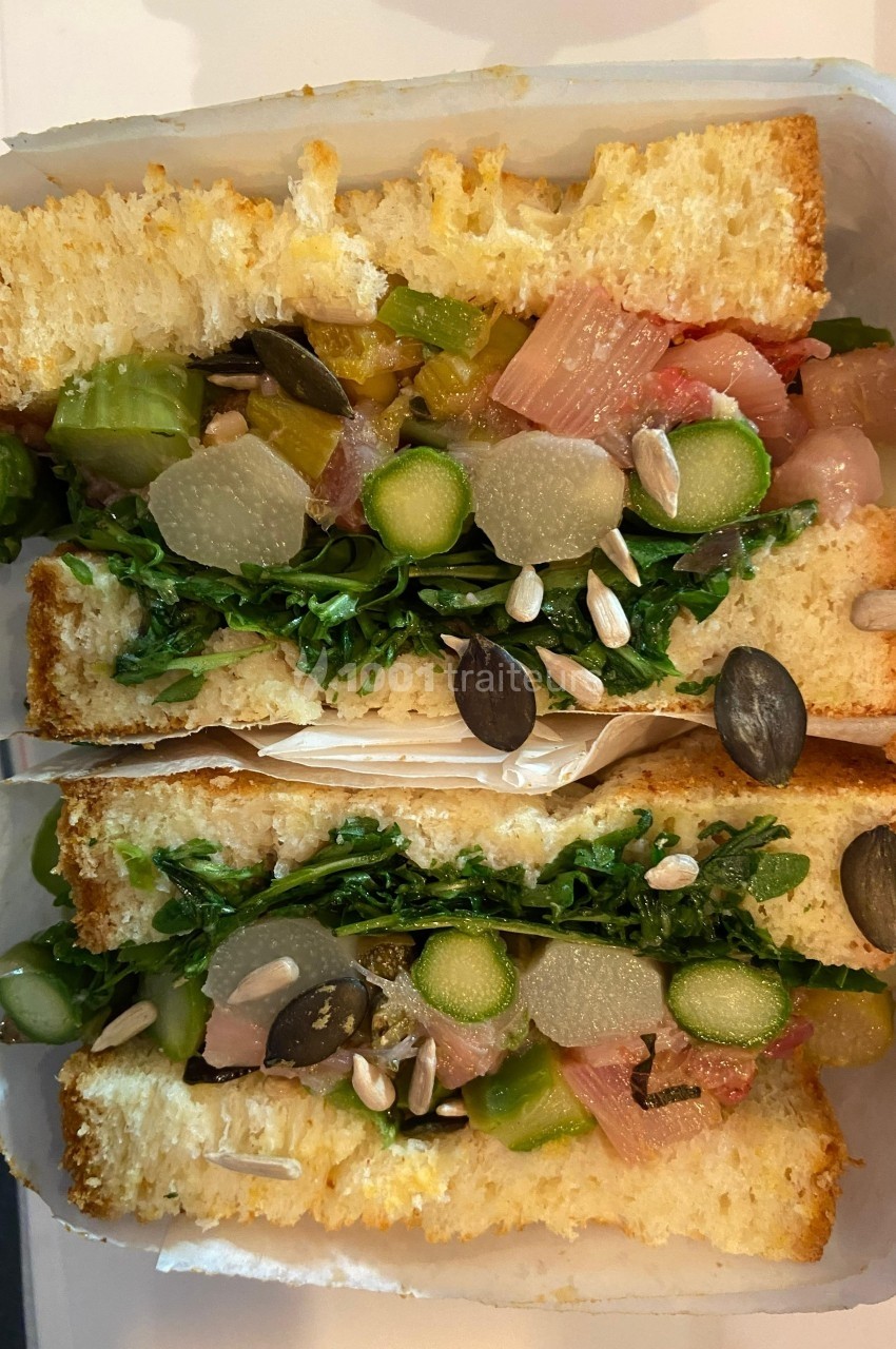 Sandwich garni de légumes frais, graines variées et pain doré, présenté en coupe transversale.