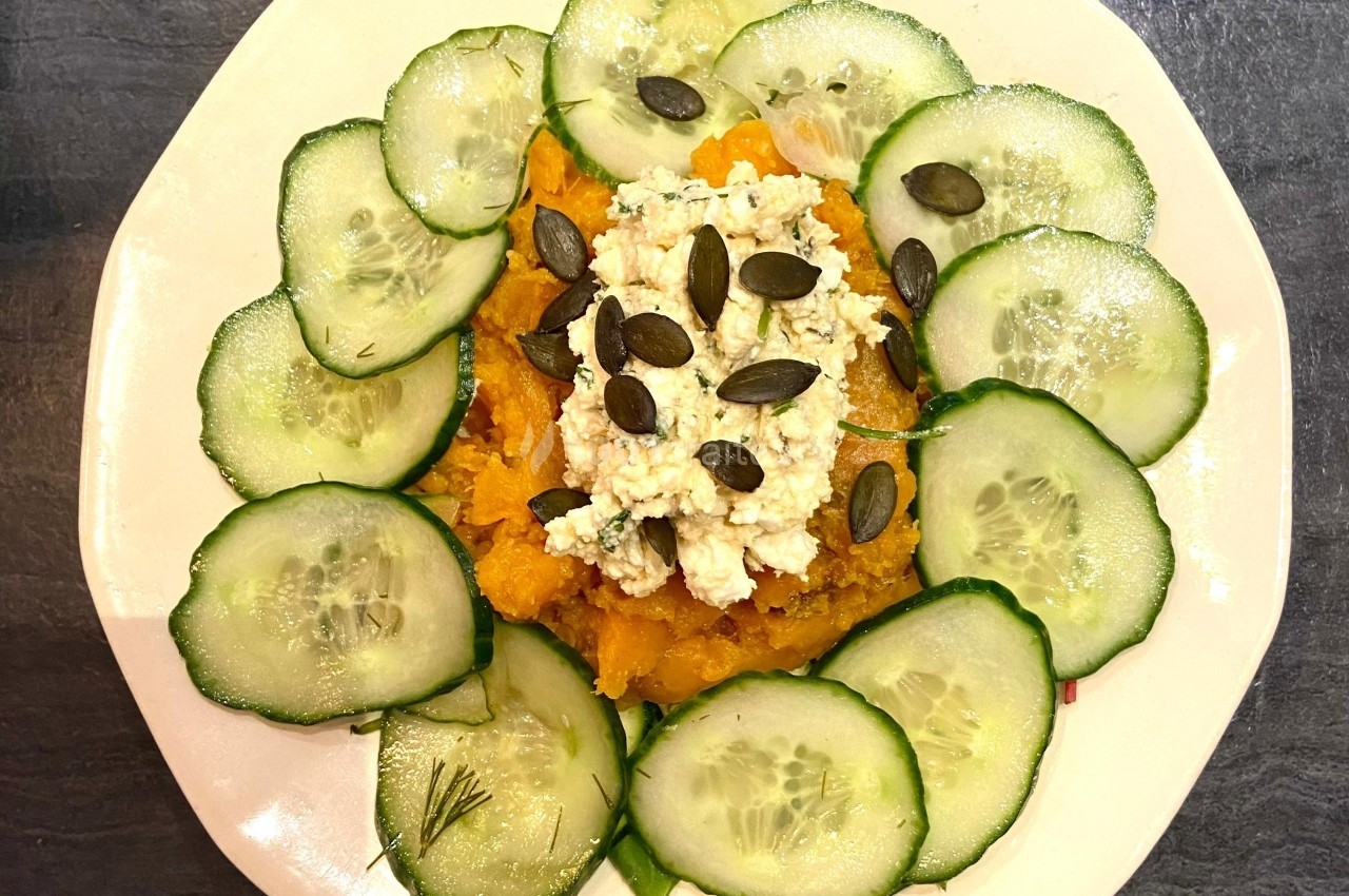 Assiette garnie de purée de légumes, fromage émietté, graines de courge et rondelles de concombre disposées en cercle.