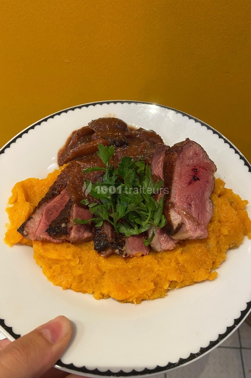 Assiette de magret de canard tranché sur purée de patates douces, garnie de persil et accompagnée d'une sauce.