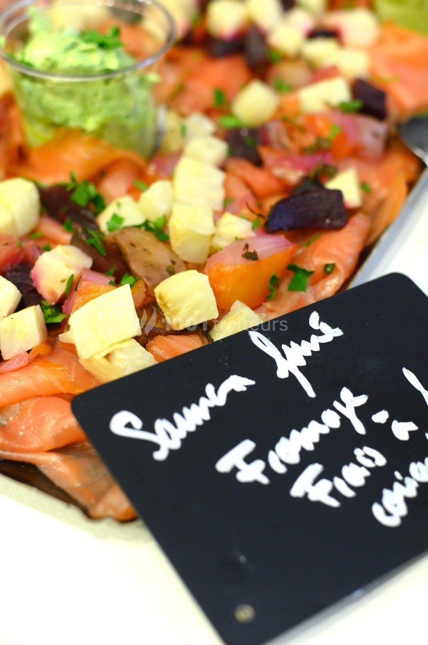 Assiette de saumon fumé garnie de dés de fromage, betteraves, herbes fraîches et une sauce verte en accompagnement.