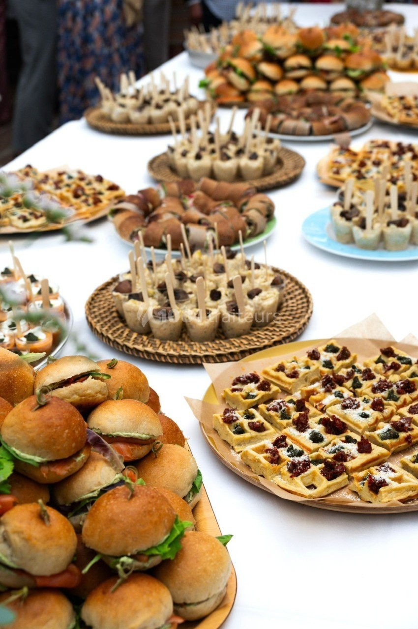 Buffet varié avec mini-burgers, gaufres garnies et amuse-bouches sur une table blanche.