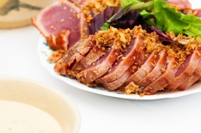 Assiette de magret de canard tranché sur purée de patates douces, garni de persil et accompagné d'une sauce.