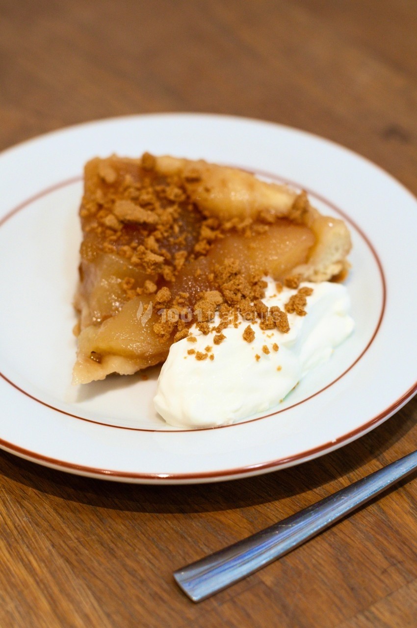 Part de tarte aux pommes caramélisées servie avec une cuillerée de crème fouettée sur une assiette blanche.