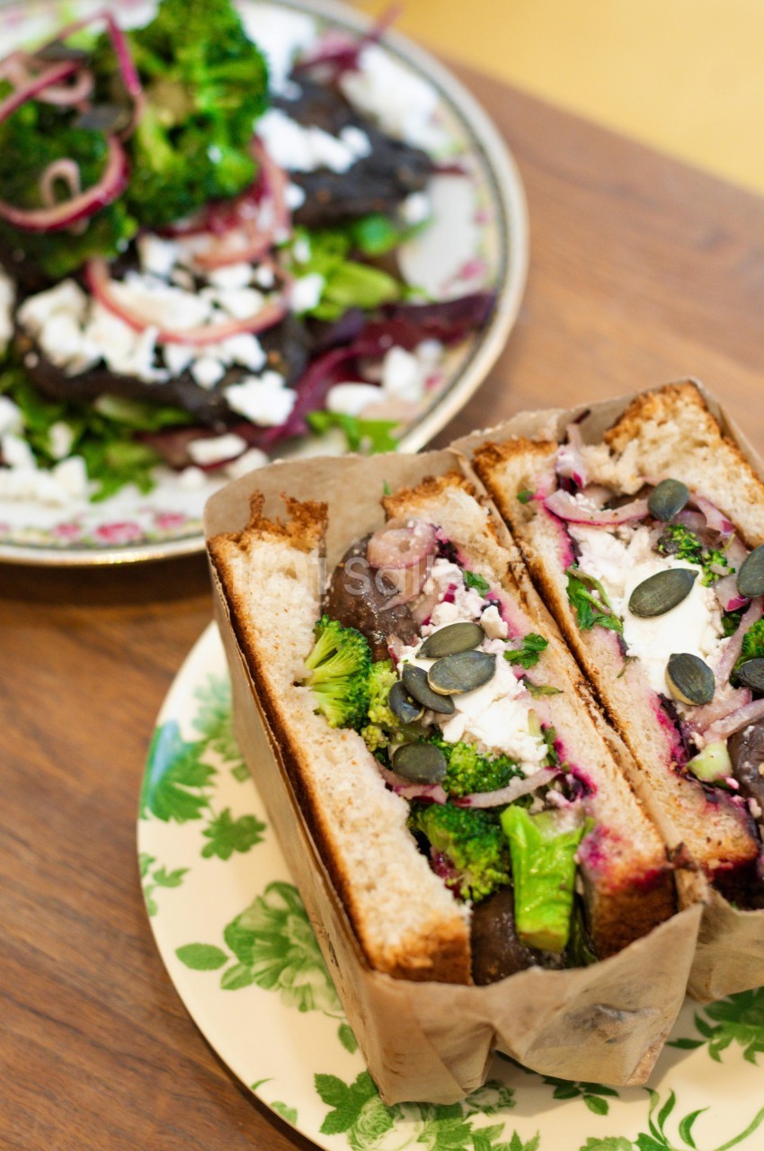 Sandwich végétarien garni de légumes, fromage et graines, accompagné d'une salade colorée sur une table en bois.