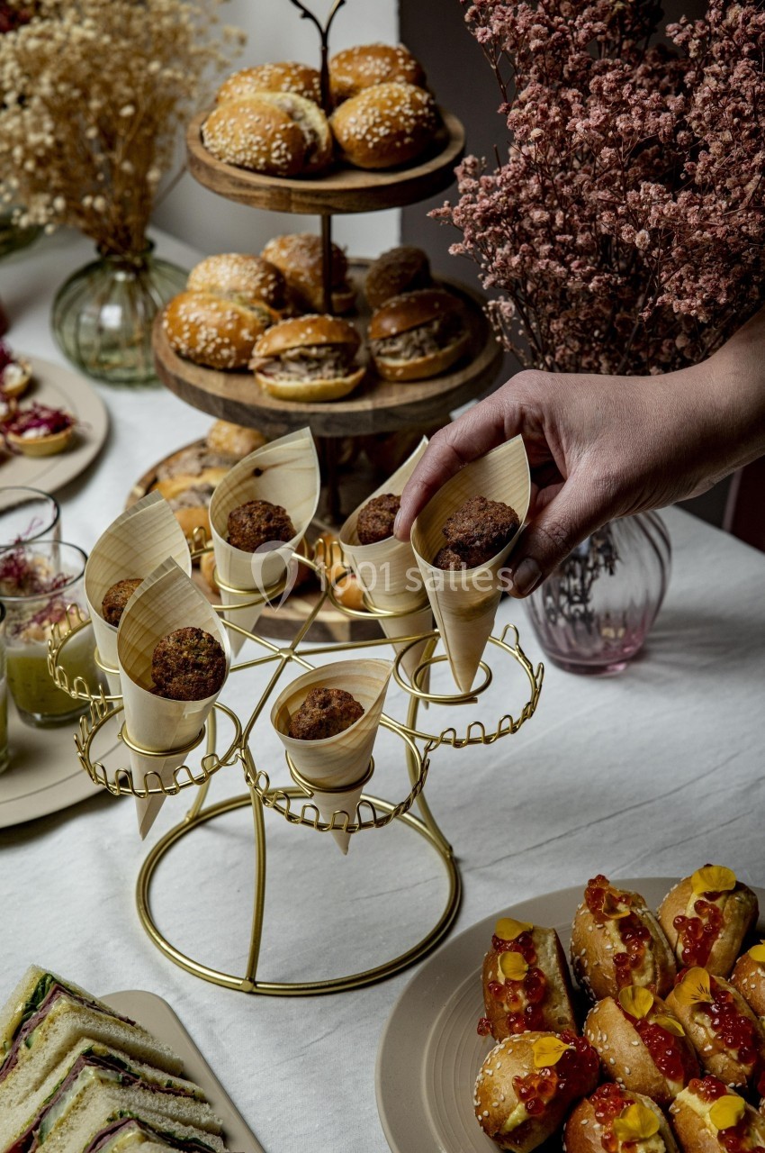 Plateau de buffet avec mini-sandwichs, amuse-bouches en cornets, et autres assortiments sur une table décorée.