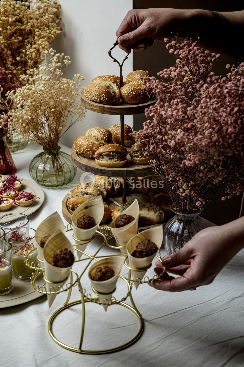 Plateau de pâtisseries et amuse-bouches disposés sur des présentoirs dorés, entourés de fleurs séchées.