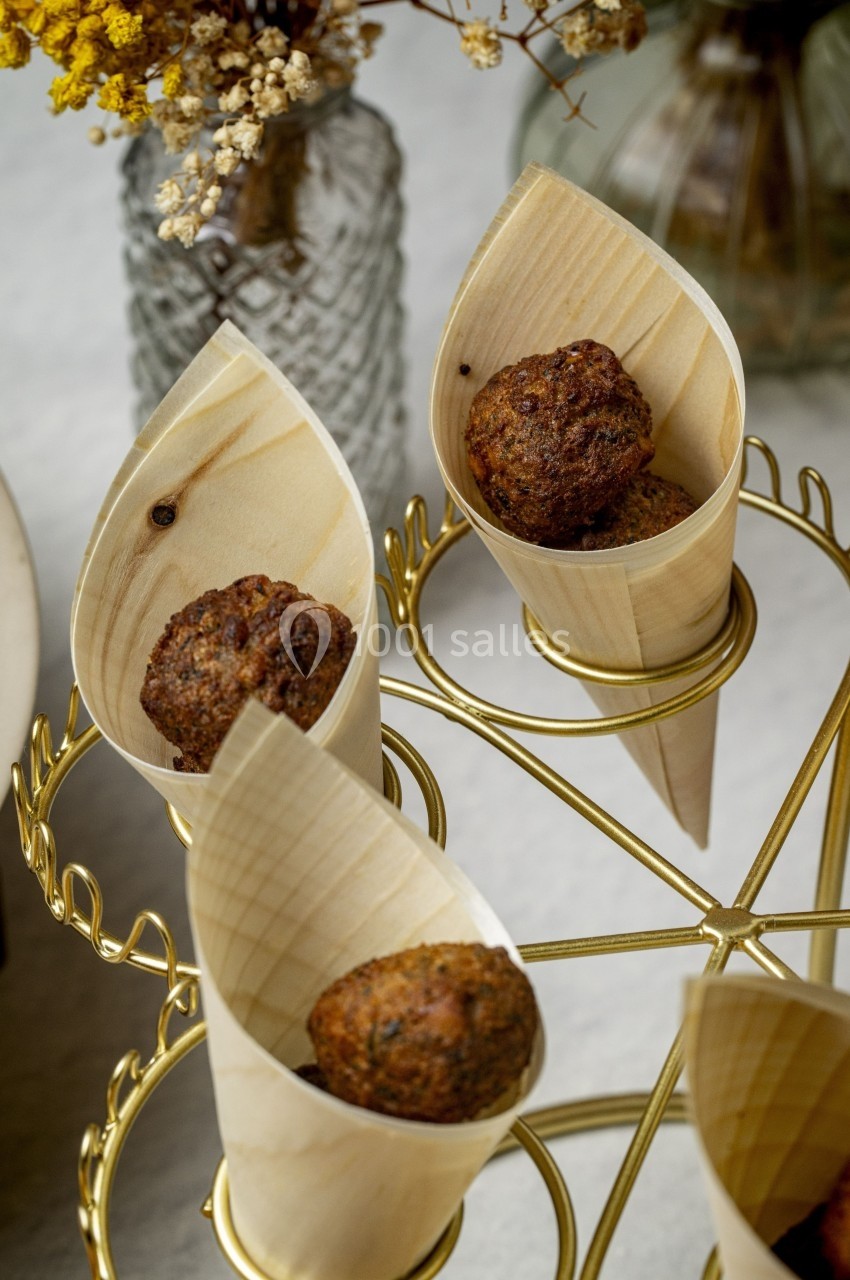 Boulettes dorées servies dans des cônes en bois, présentées sur un support doré avec des fleurs en arrière-plan.