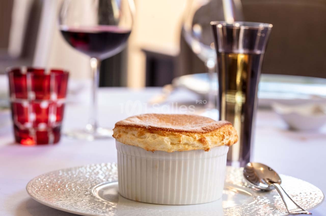 Soufflé doré servi dans un ramequin blanc sur une table dressée avec des verres de vin et d'eau.