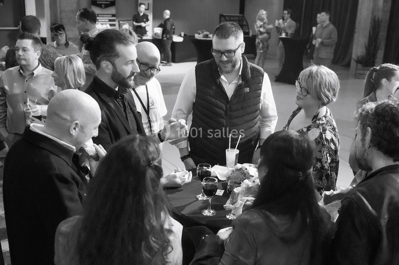 Un groupe de personnes discute autour d'une table haute lors d'un événement convivial en intérieur.
