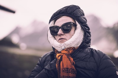 Femme assise dans une lumière tamisée, entourée de verres, regardant vers l'objectif.