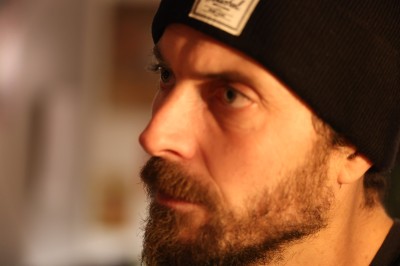 Femme assise dans une lumière tamisée, entourée de verres, regardant vers l'objectif.