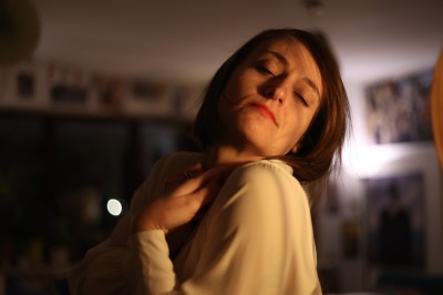 Femme assise dans une lumière tamisée, entourée de verres, regardant vers l'objectif.