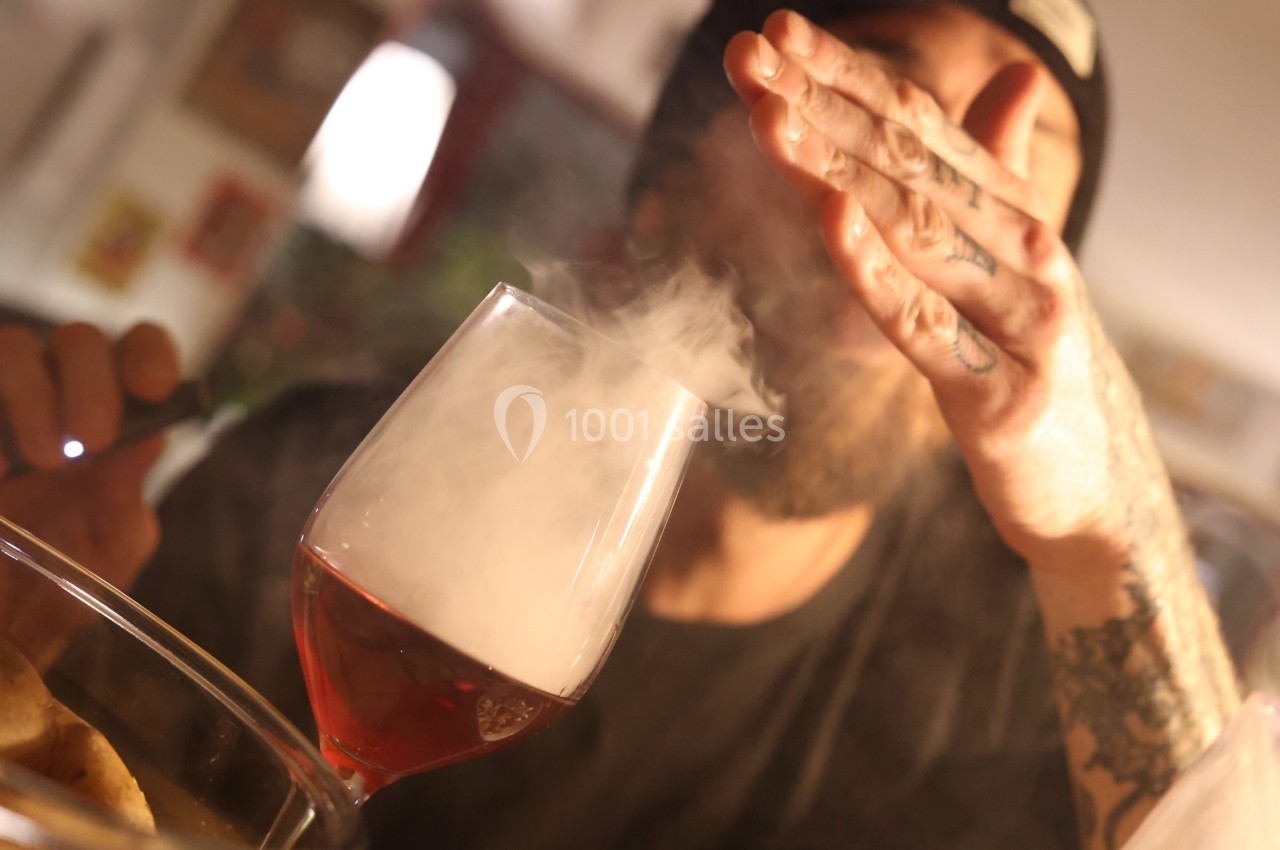 Un homme souffle de la vapeur au-dessus d'un verre de vin rouge dans un environnement intérieur chaleureux.