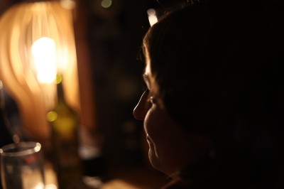 Femme assise dans une lumière tamisée, entourée de verres, regardant vers l'objectif.