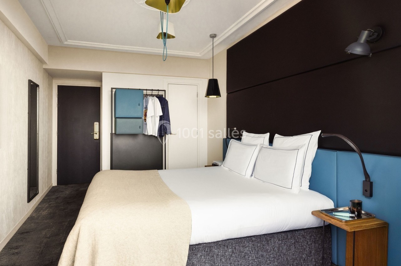 Chambre d'hôtel moderne avec lit double, linge blanc, mur sombre, éclairage suspendu et penderie ouverte.