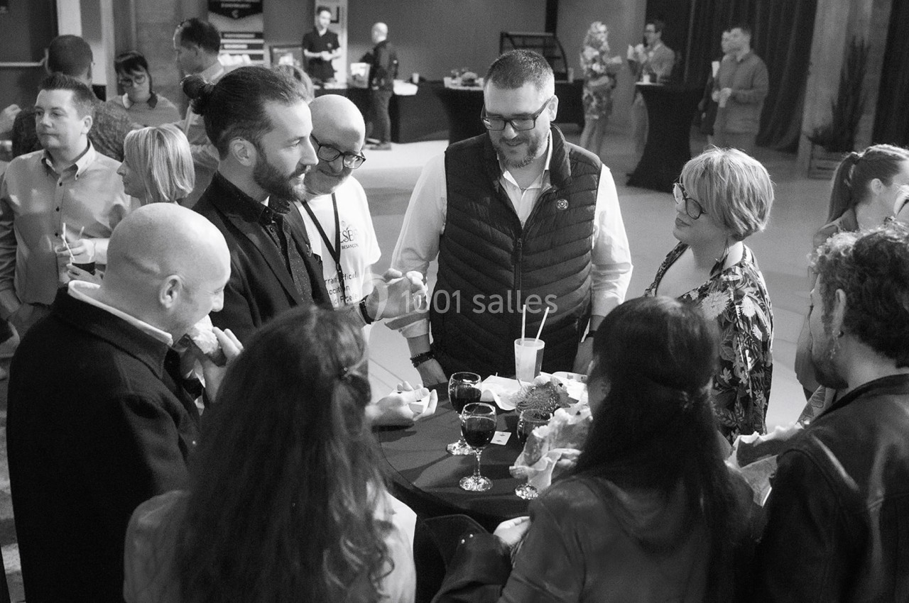 Groupe de personnes discutant autour d'une table haute lors d'un événement convivial en intérieur.