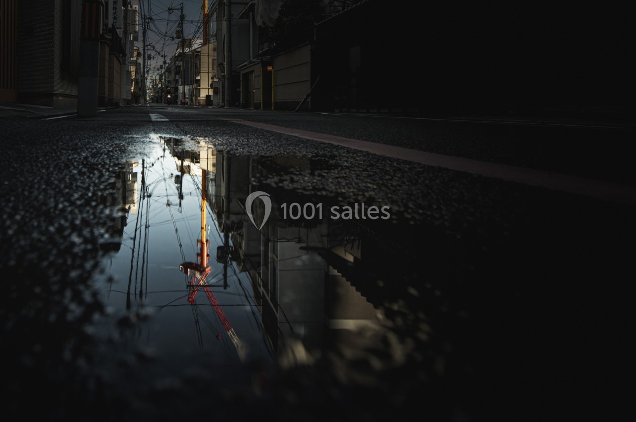 Reflet d'une grue et de bâtiments dans une flaque d'eau sur une rue sombre en milieu urbain.